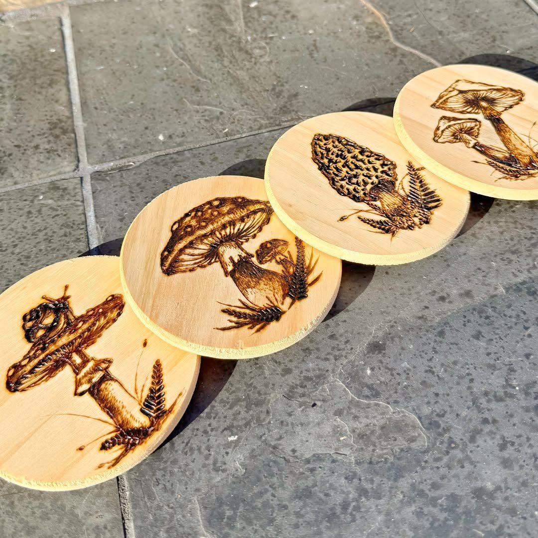Wooden coasters with burned mushroom and fern designs on a grey stone floor.