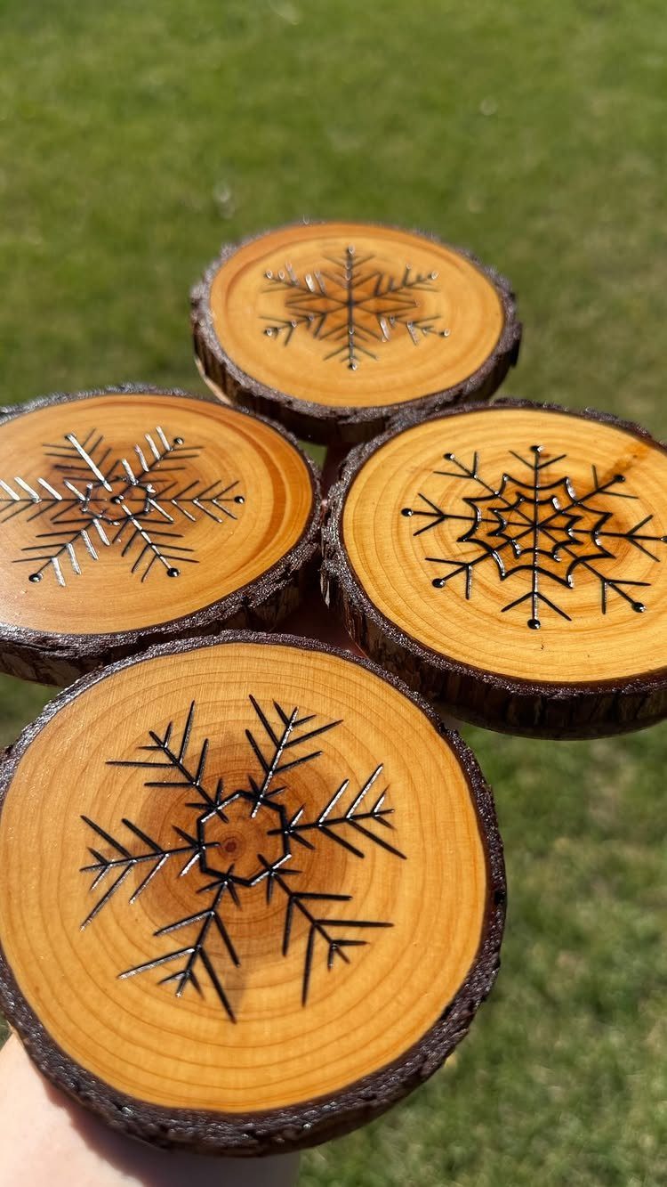 Wood slice coasters with burned snowflake designs resting on green grass.