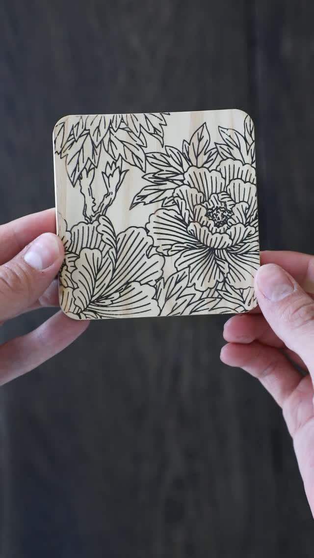 Wooden coaster with a detailed burned floral design held by two hands.
