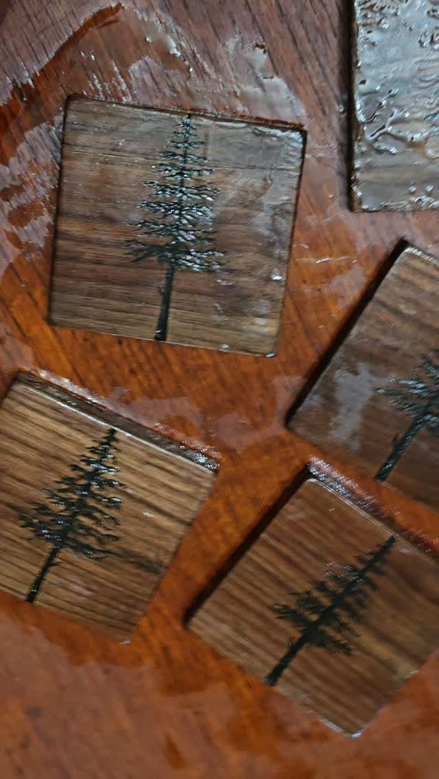 Wooden coasters with pyrography pine tree designs on a wet wooden table