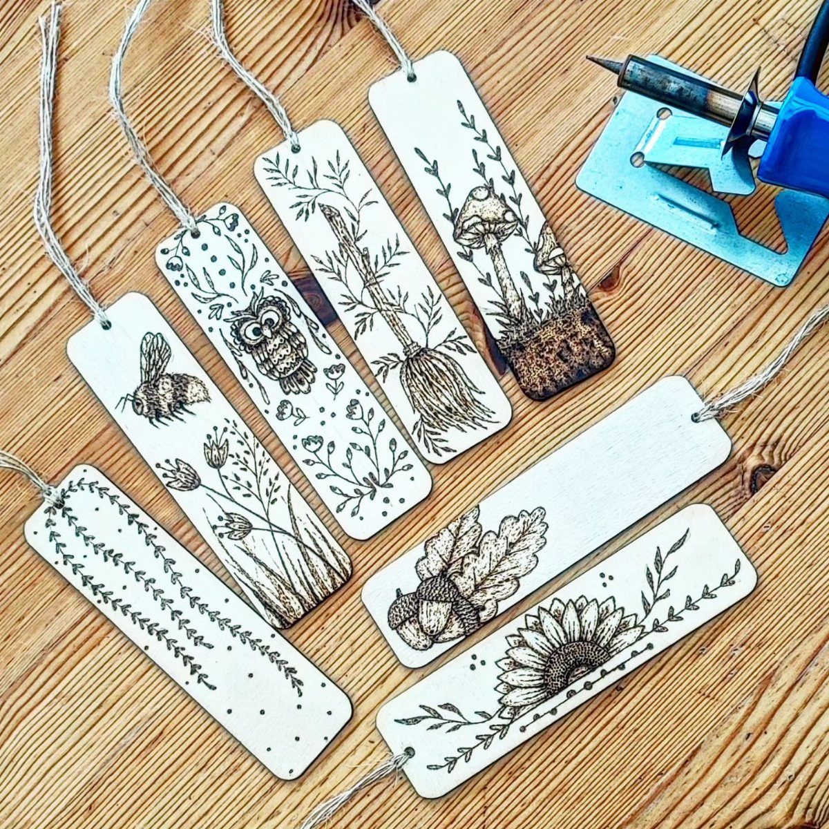 Wooden bookmarks with burned nature illustrations and a wood-burning tool on a table.