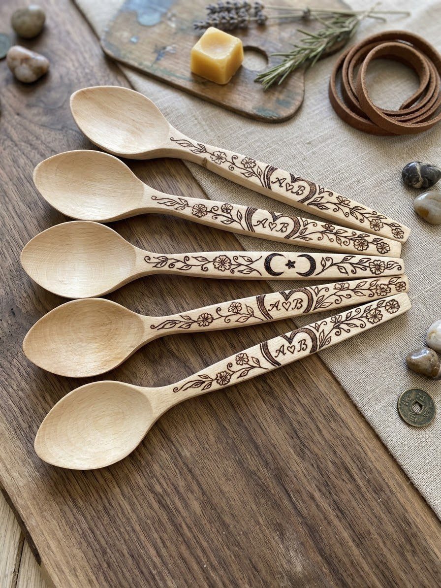 Wooden spoons with detailed wood-burned floral designs and initials on a rustic table.