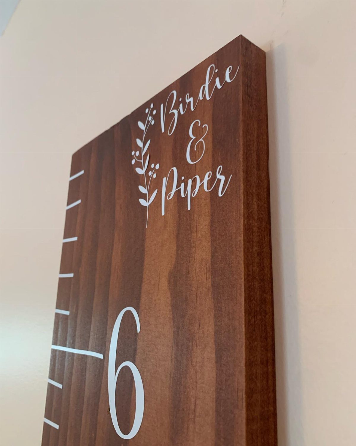 Wooden growth chart with white measurement markings and names Birdie and Piper on it.