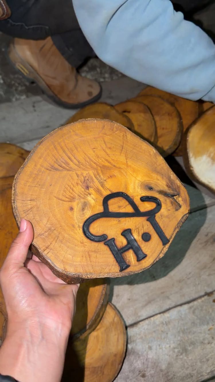 Wood slice with a dark burned-in letter H design held by a hand
