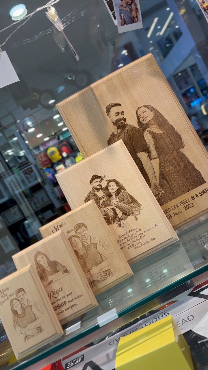Wooden plaques with detailed burned-in portraits of couples displayed on a glass shelf.
