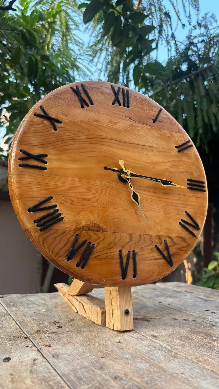 Wooden clock with burnt Roman numerals resting on a rustic wooden table outdoors
