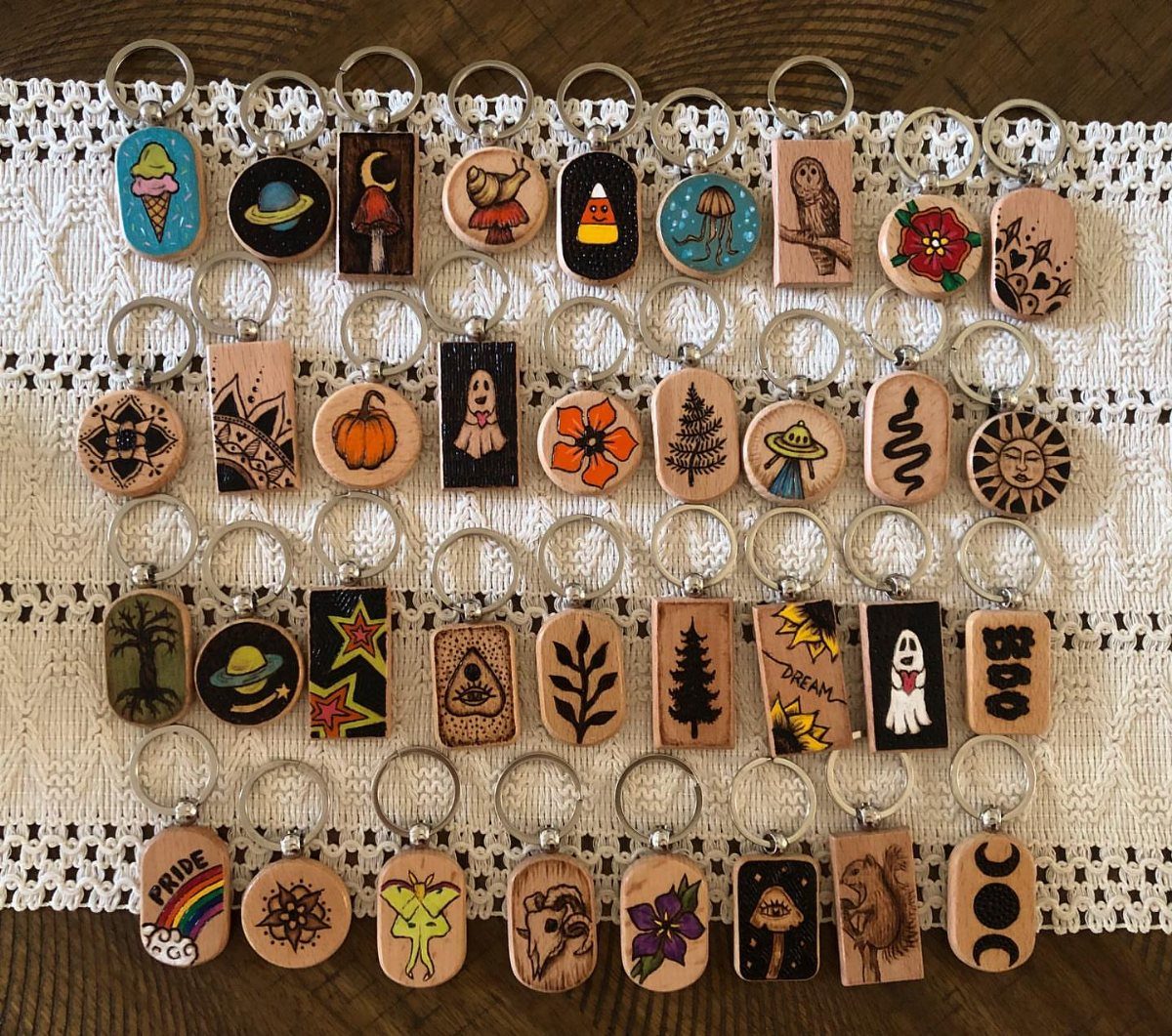 Wooden keychains with burned designs arranged on a white lace fabric background.