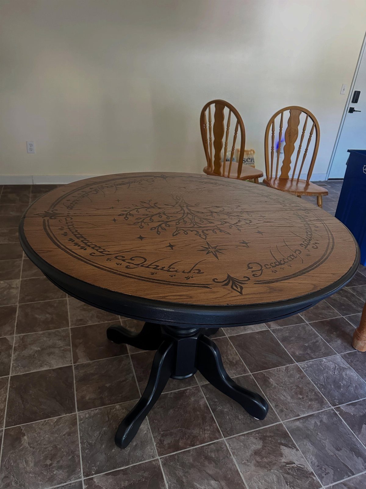 Round wooden table with intricate wood-burned floral designs and cursive text on top.