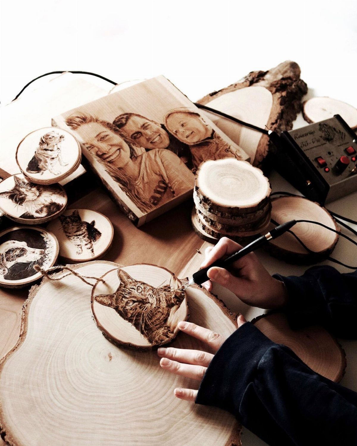 Person wood burning a cat portrait on a wooden slice among other artworks.