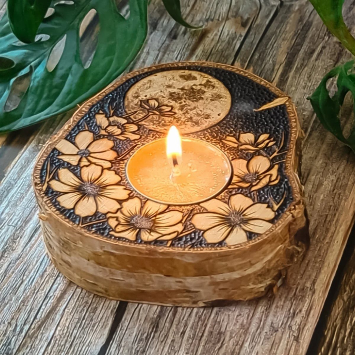 Wood slice candle holder with burned floral designs and a lit tea light