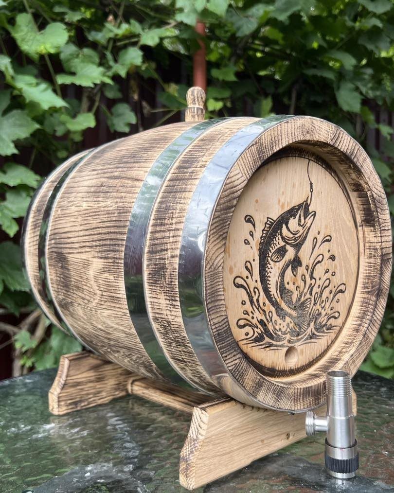 Wooden barrel with a wood-burned fish illustration resting on a wooden stand.