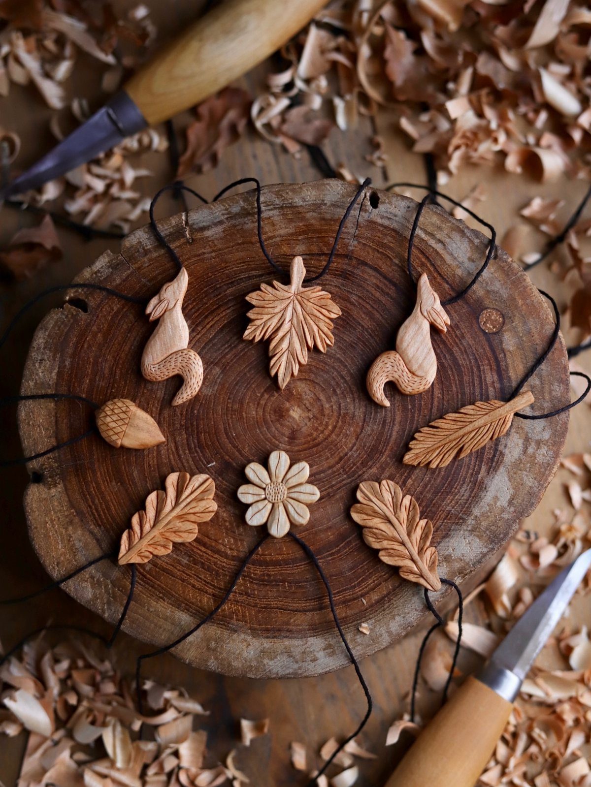Wood Carved Ornaments: 7 Ideas for Holiday and Home 4 Hand-carved wooden animal and plant pendants resting on a rustic wood slice with shavings.
