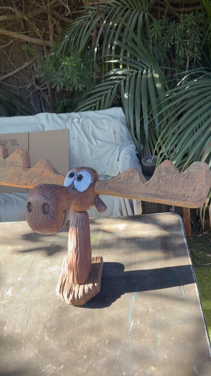 Wood Carving Animals: 14 Ideas to Try With a Knife 3 Carved wooden moose with large antlers and wide eyes standing on a grey surface.