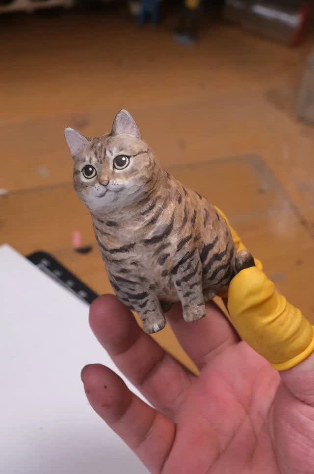 Wood Carving Animals: 14 Ideas to Try With a Knife 2 Small carved wooden tabby cat with a plump body held by a person's fingers.