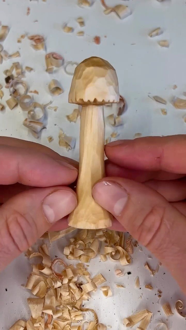 Hand-carved wooden mushroom figurine held by hands amidst light wood shavings.