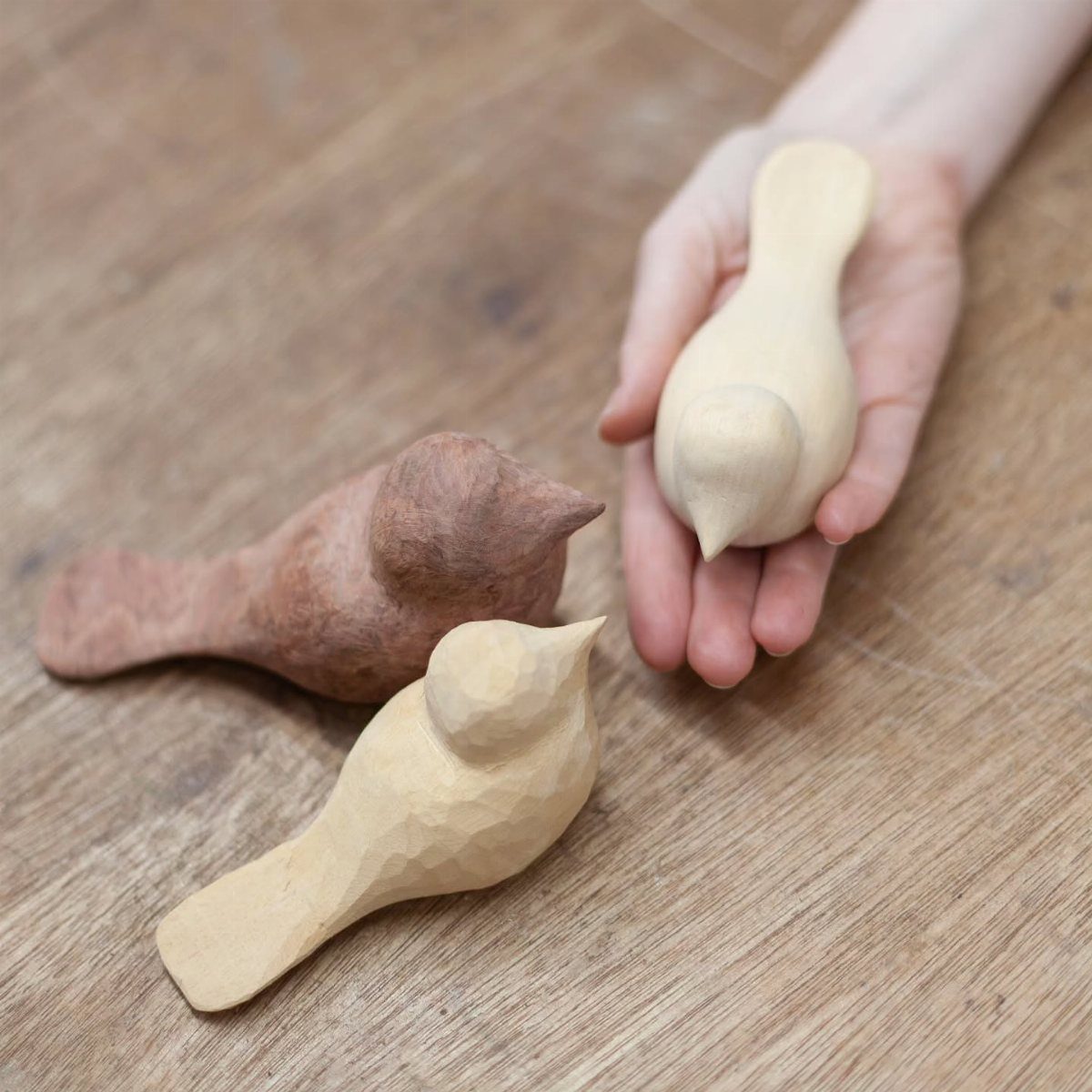 Three small hand-carved wooden birds resting on a light wood tabletop.