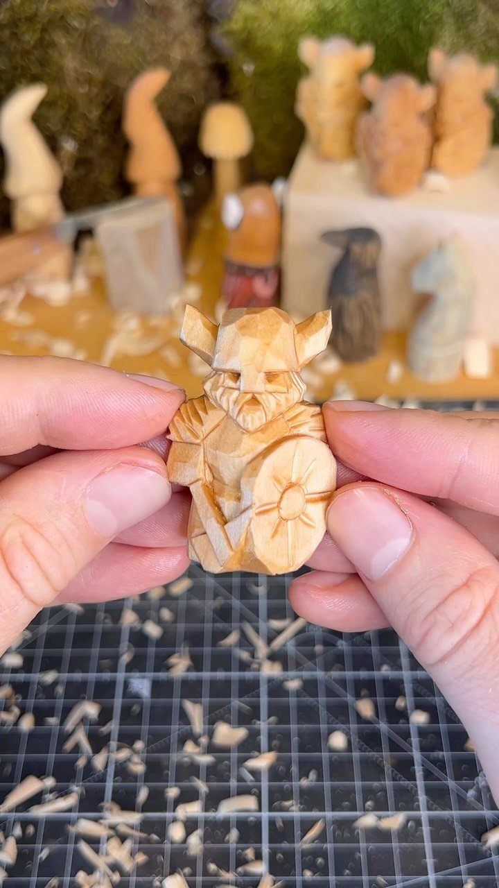 Small hand-carved wooden warrior figure held by hands with other carvings behind.