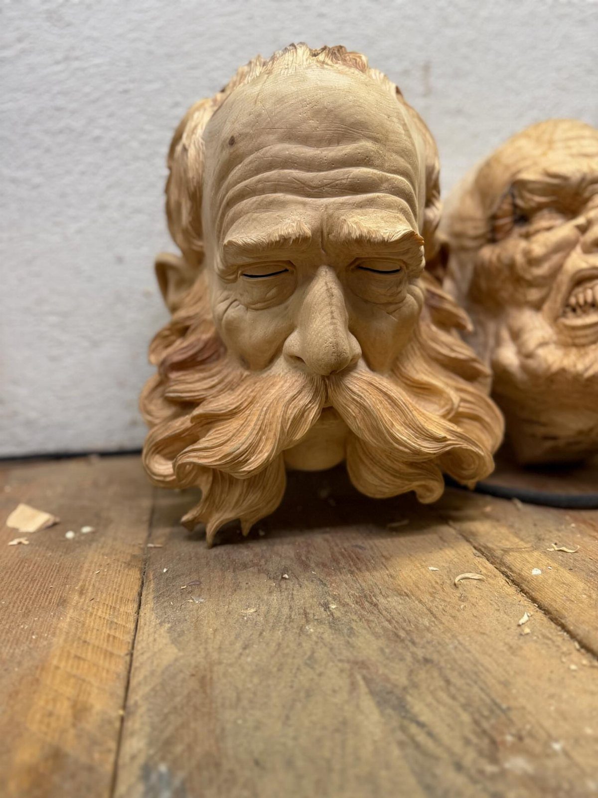 Detailed wood carvings of elderly men with beards on a wooden workbench
