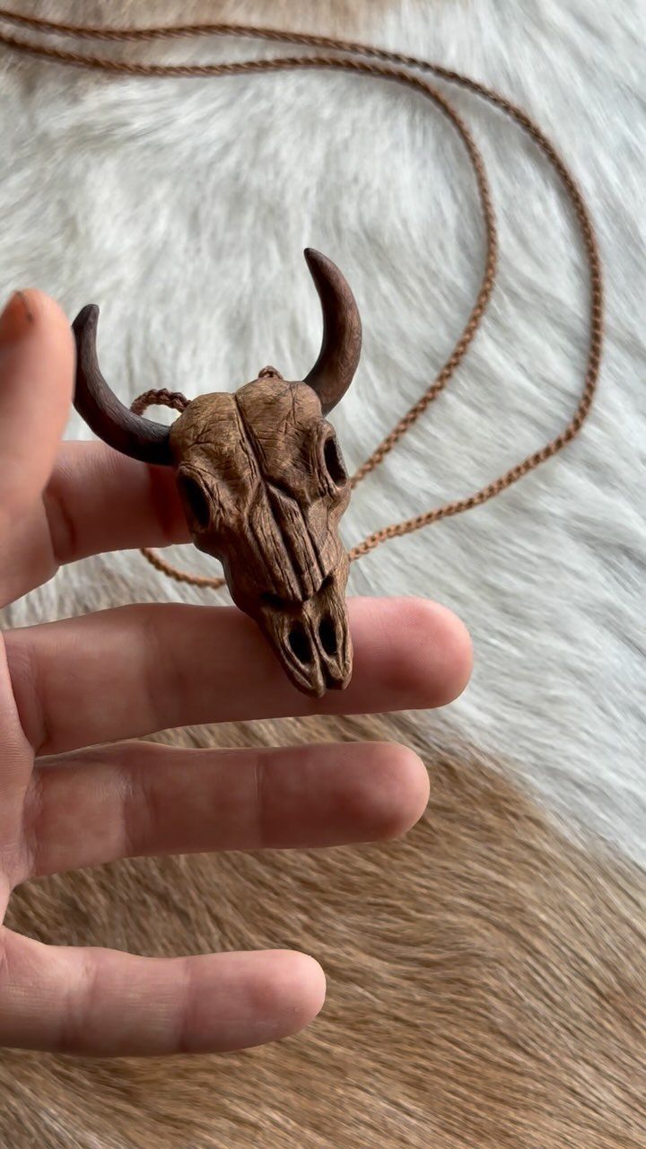 Wooden carved animal skull pendant on a leather cord held by a hand.