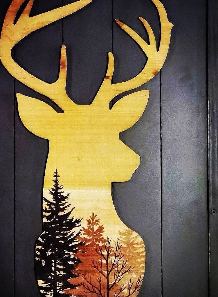 Wooden deer head cutout with a forest silhouette mounted on a dark wall