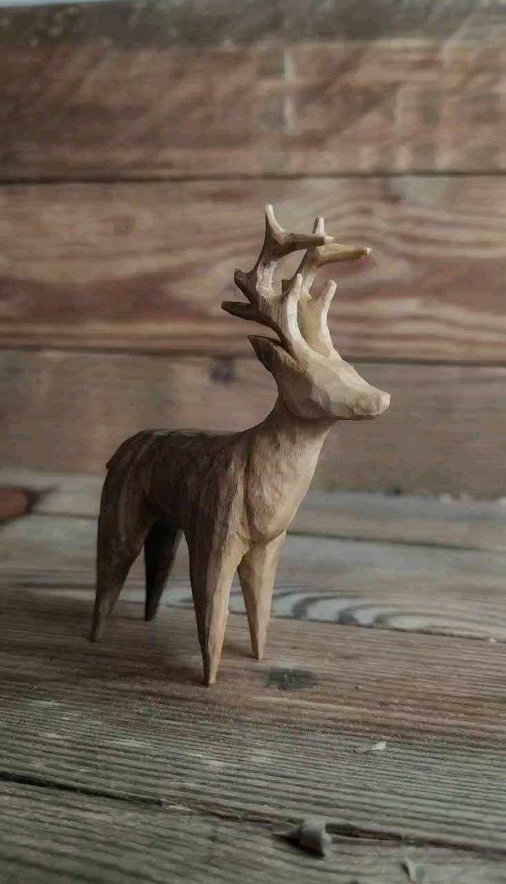 Wooden deer figurine with detailed antlers standing on a rustic wooden surface.