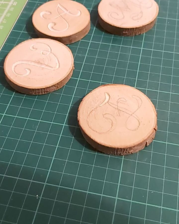 Wood Carving for Beginners: 10 Ideas to Try First 6 Four circular wooden slices with carved cursive letters on a green cutting mat.