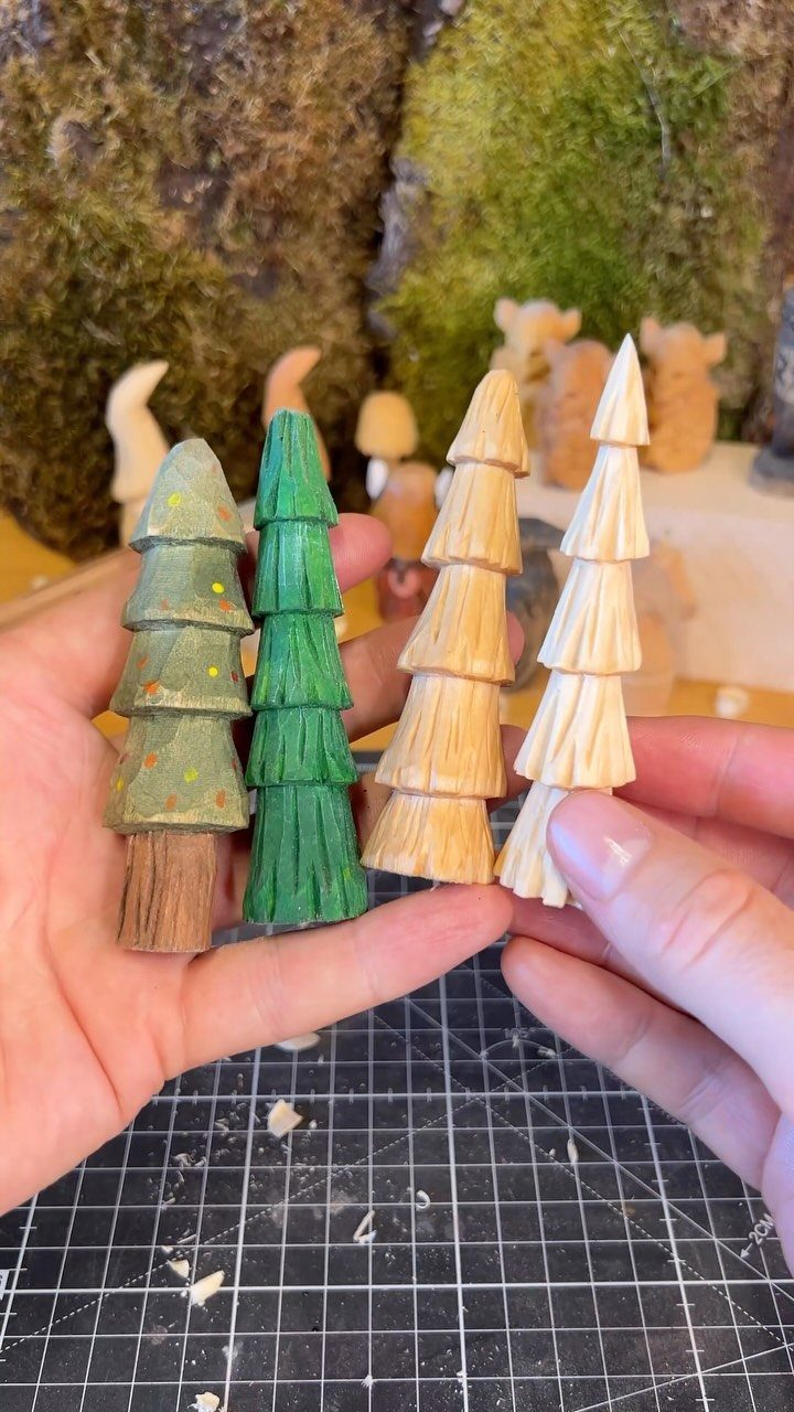 Wood Carving for Beginners: 10 Ideas to Try First 8 Hand-carved wooden pine trees held in hands over a grey cutting mat.