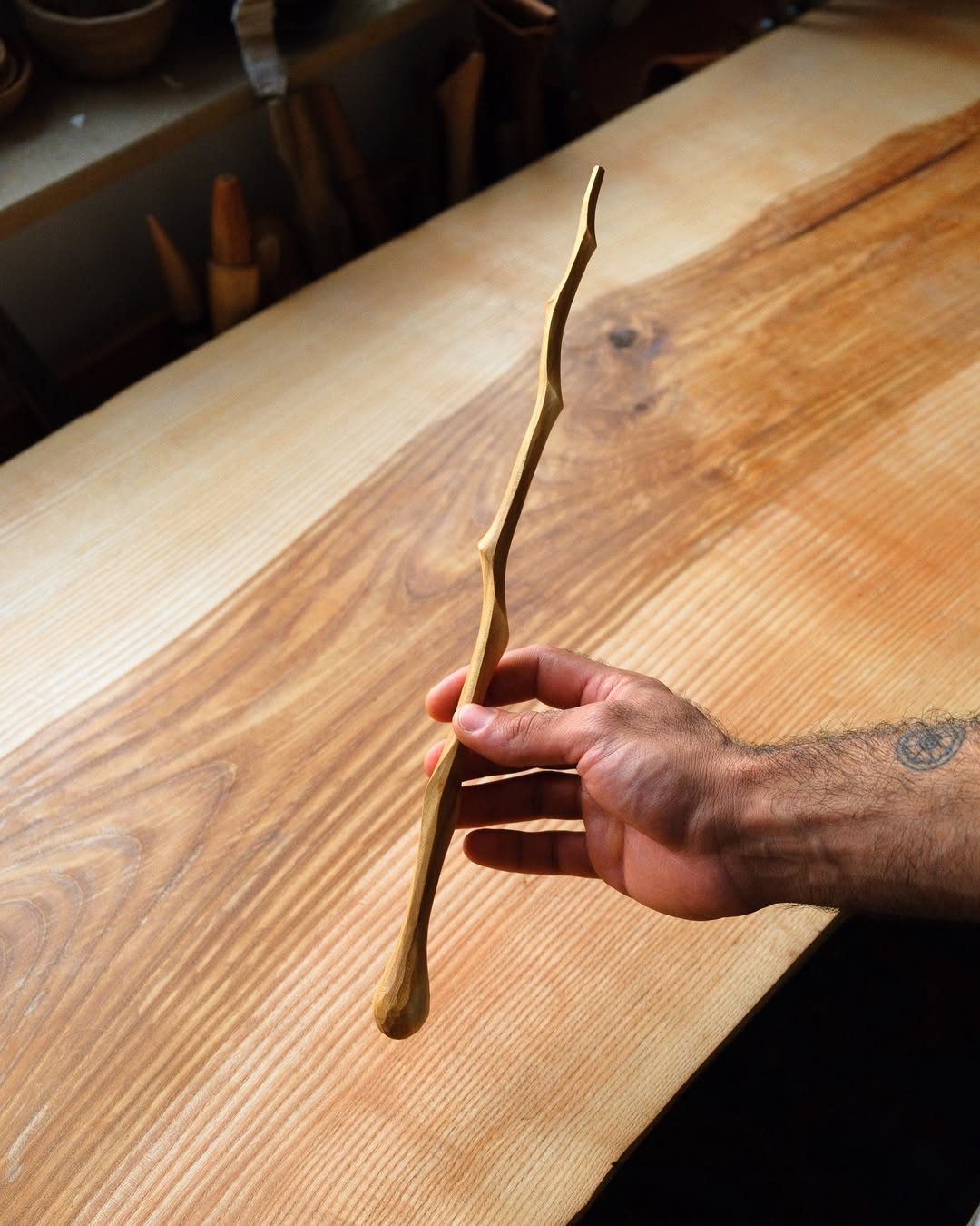Wood Carving for Beginners: 10 Ideas to Try First 10 Hand-carved wooden stick with organic curves held against a natural wood tabletop.