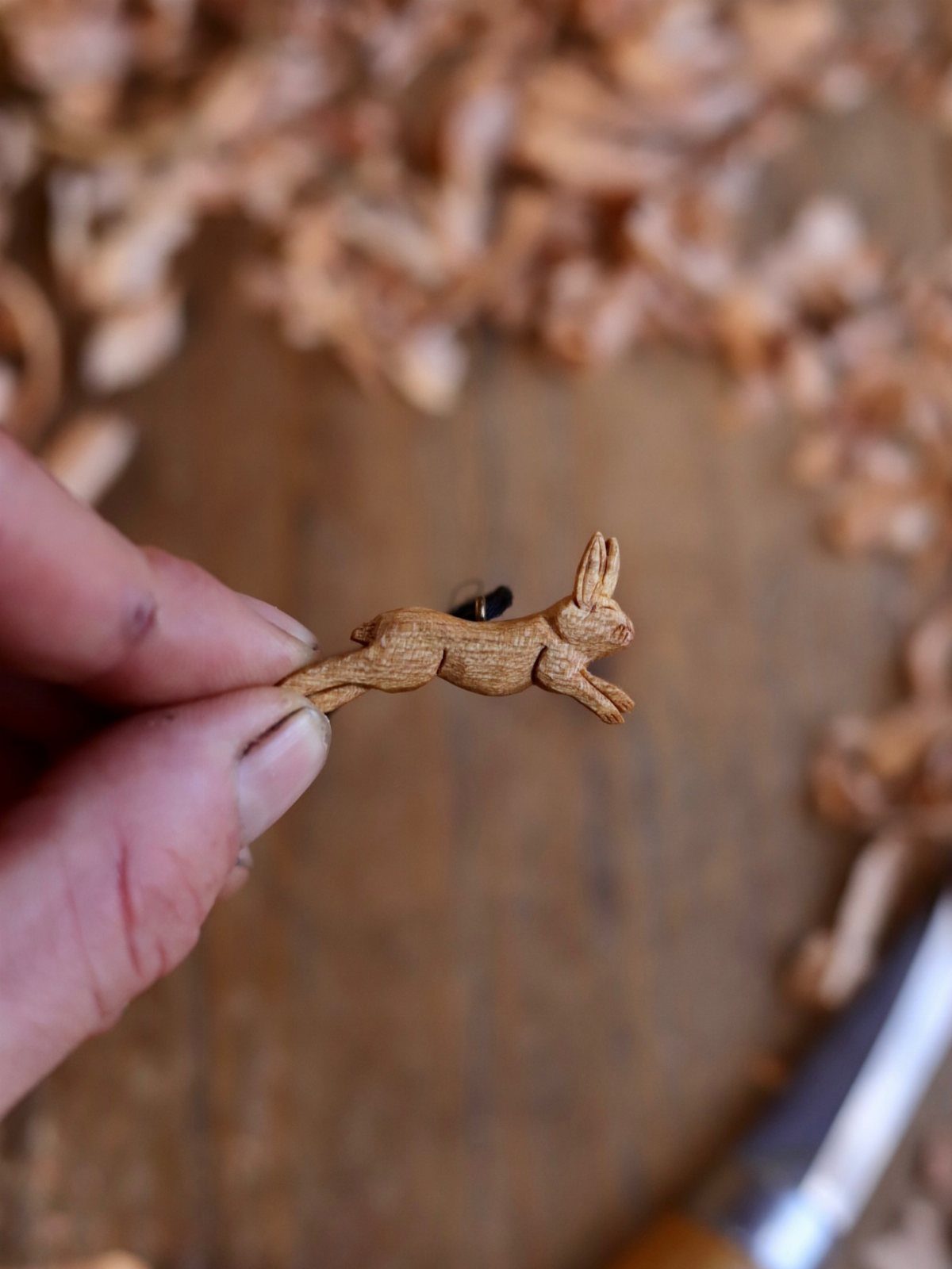 Wood Carving for Beginners: 10 Ideas to Try First 4 Small hand-carved wooden rabbit held over a surface of light brown wood shavings.