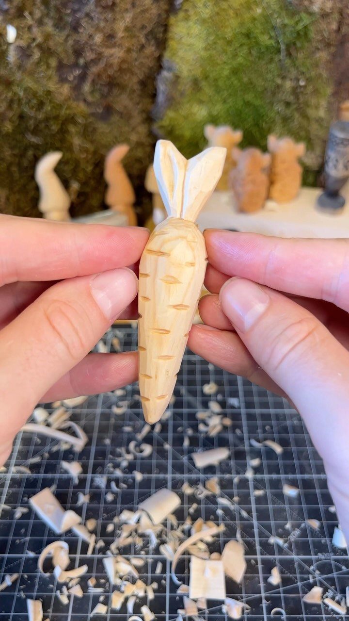 Wood Carving for Beginners: 10 Ideas to Try First 9 Hand-carved wooden carrot held by fingers over a mat with wood shavings