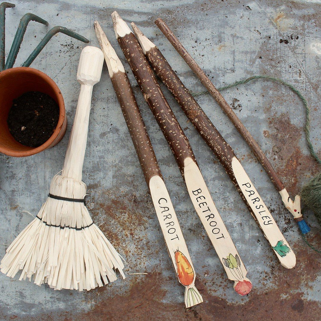 Wood Carving for Beginners: 10 Ideas to Try First 3 Hand-carved wooden garden markers and a small broom on a metal surface.