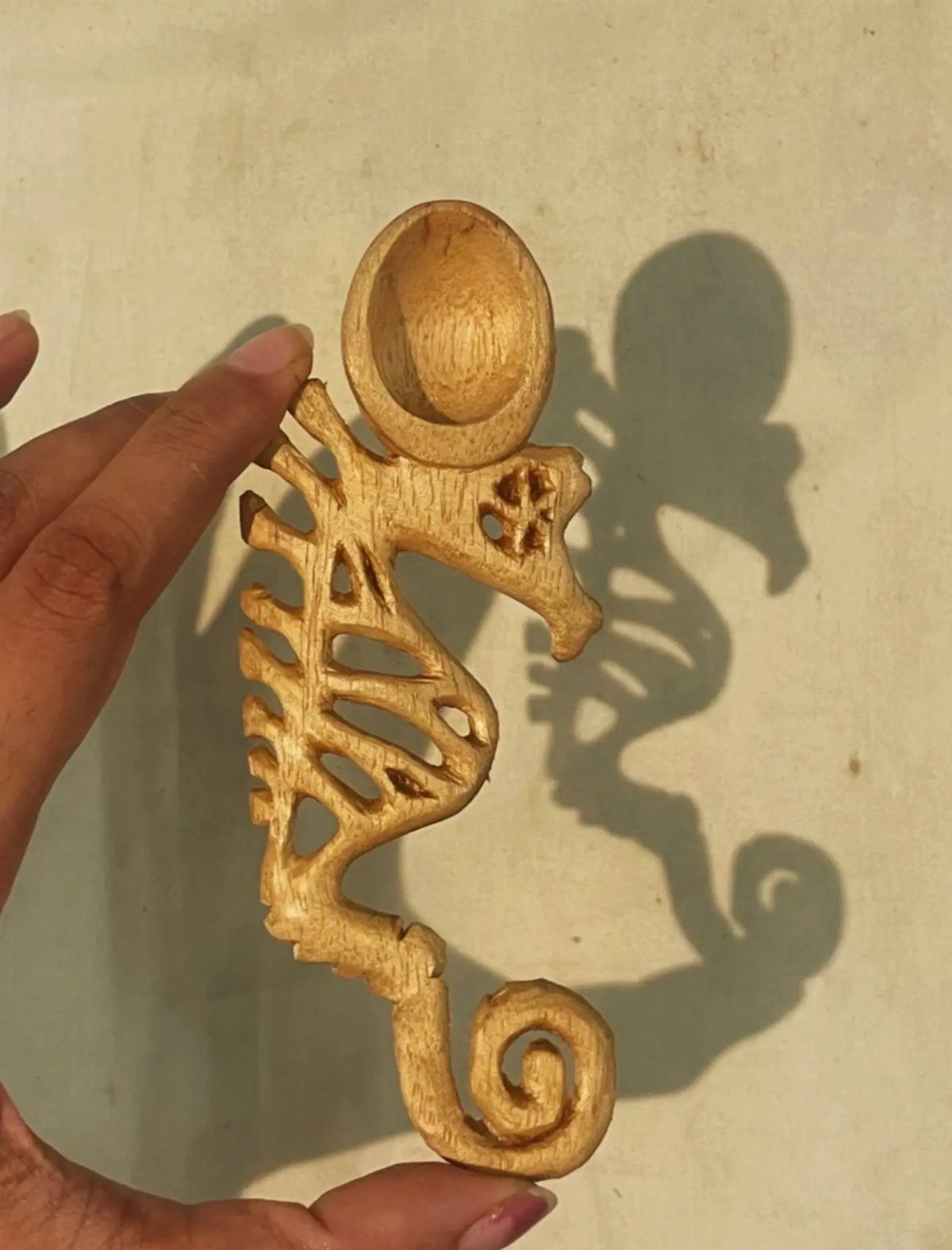 Wooden seahorse carving with intricate openwork patterns held by a person's hand.