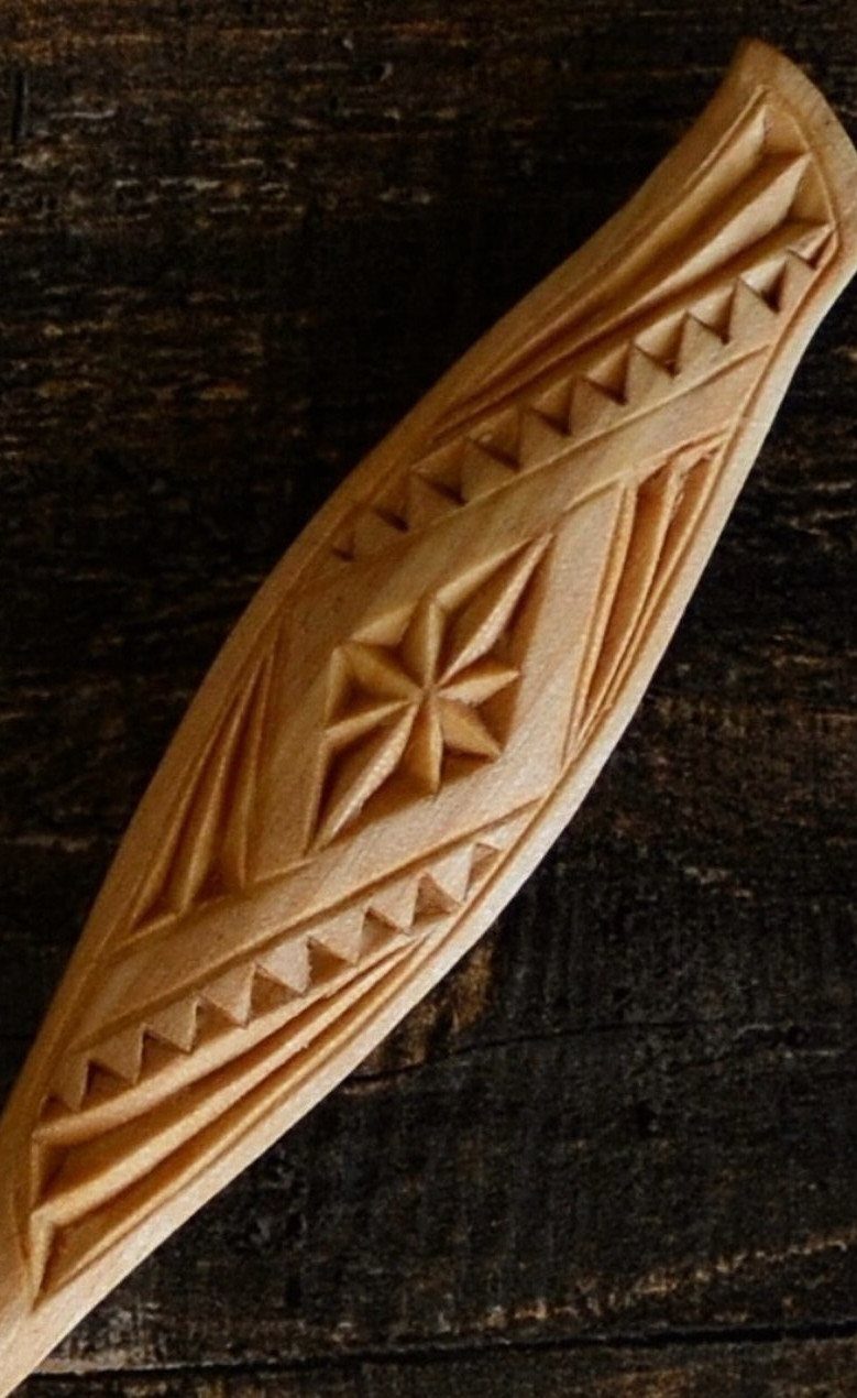 Carved wooden handle with a geometric starburst and triangular patterns on dark wood.