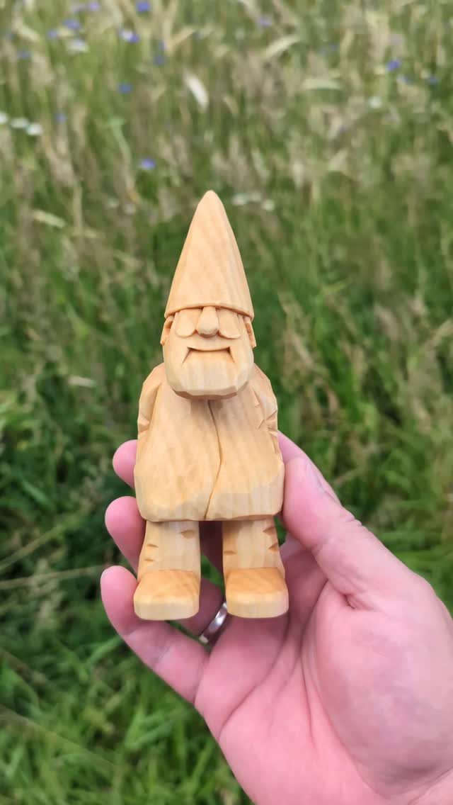 Wooden gnome carving with a pointed hat held in a person's hand outdoors.