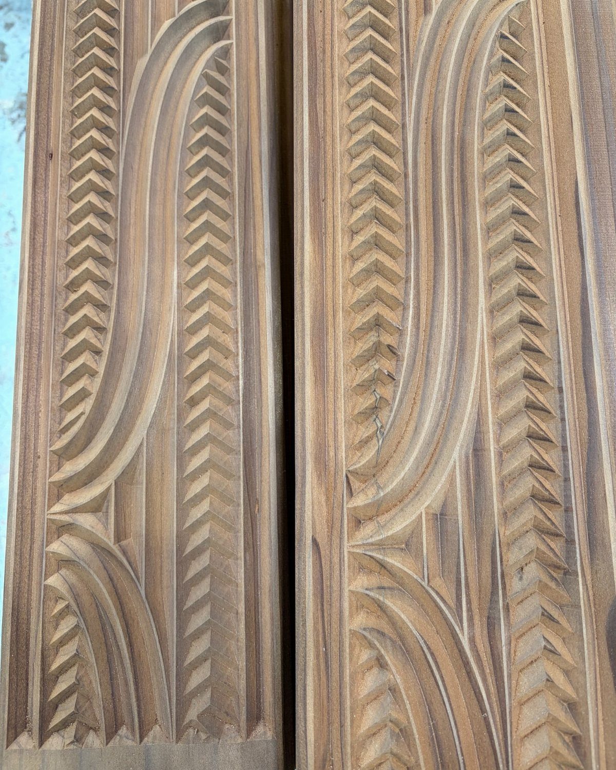 Intricate wood carving patterns with curved lines and chevron notches on brown planks.