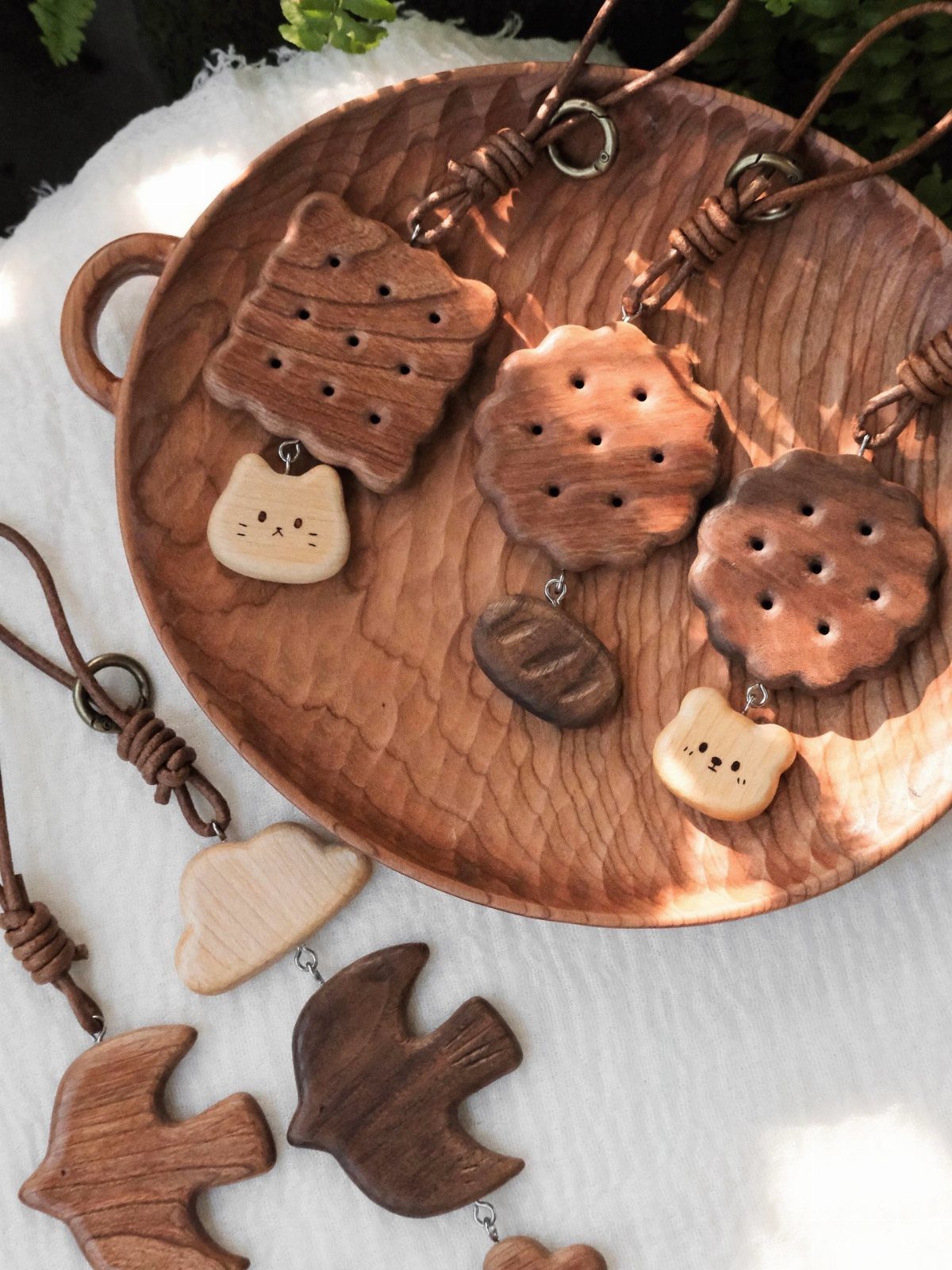Hand-carved wooden charms and keychains in various shapes resting on a wooden tray.