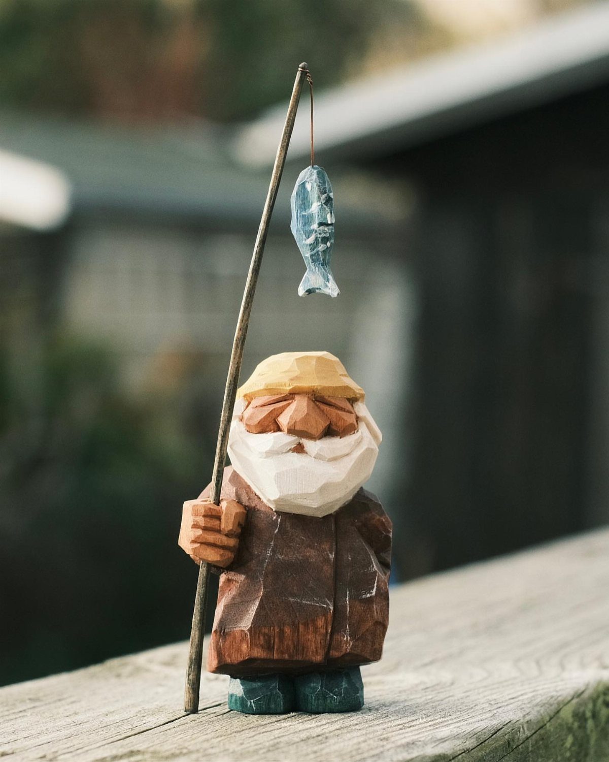 Carved wooden fisherman figurine holding a fishing pole with a small blue fish.