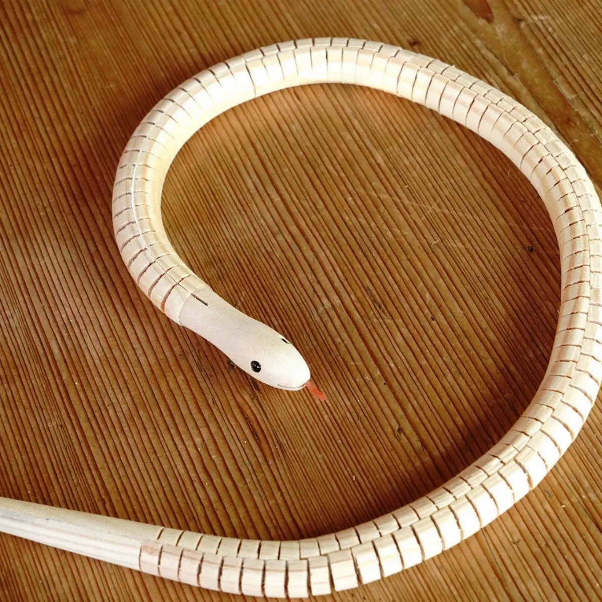 6 Wood Carving Snake Ideas for Every Skill Level 3 Articulated wooden snake sculpture with interlocking segments resting on a light wood surface.