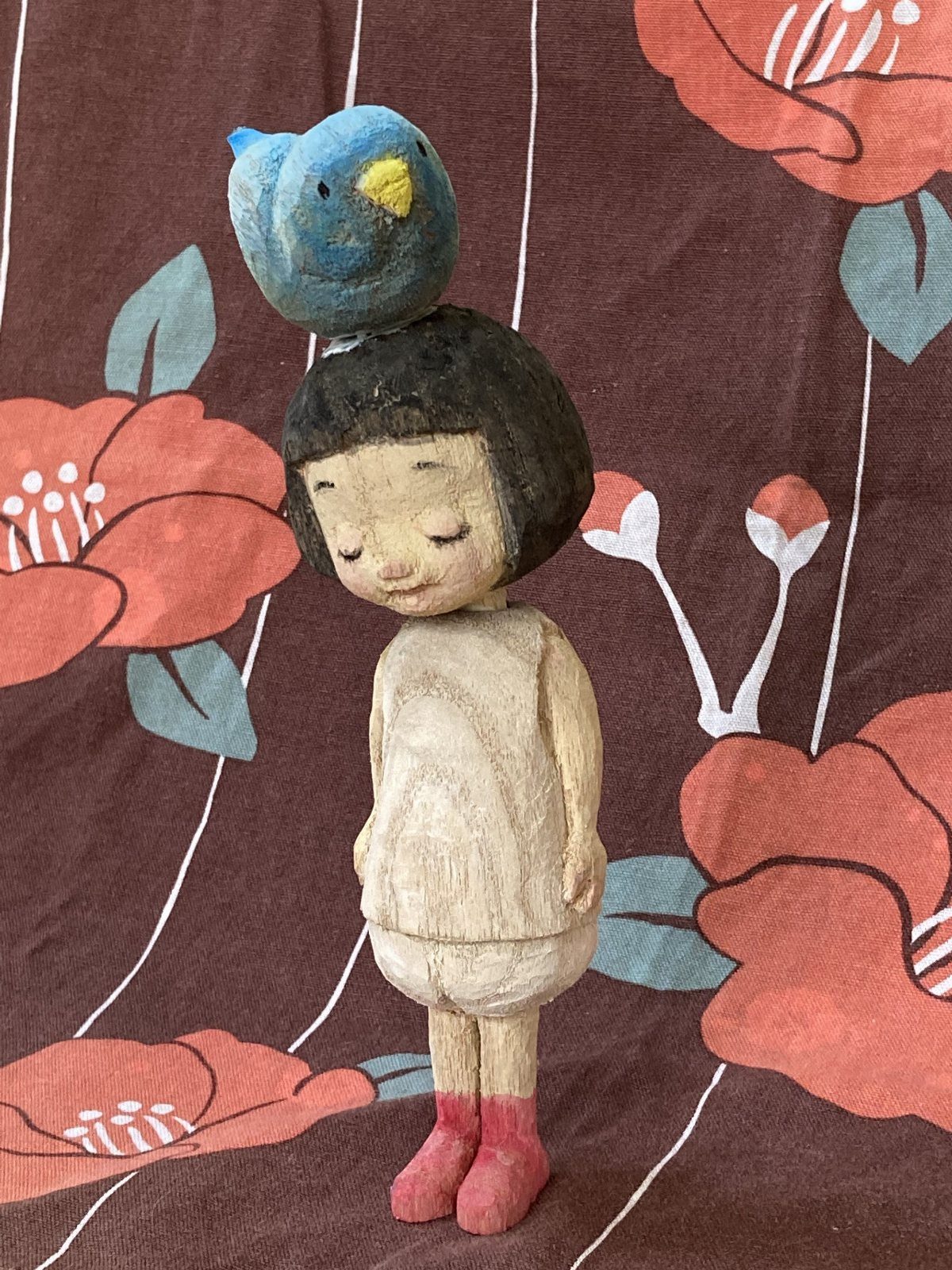 Carved wooden doll of a girl with a blue bird on her head.
