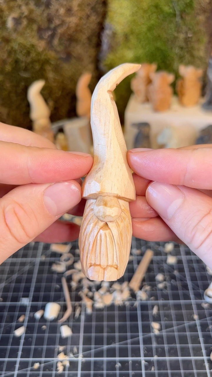 Hand-carved wooden gnome figurine held by hands over a workspace with wood shavings.