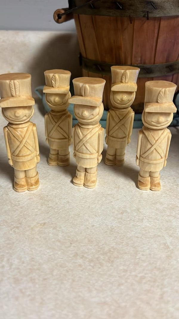 Five hand-carved wooden toy soldiers in uniforms standing on a light surface.
