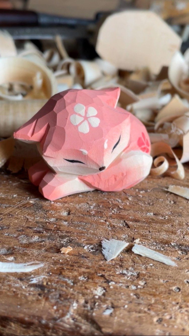 Pink carved wooden fox figurine resting on a workbench with wood shavings.