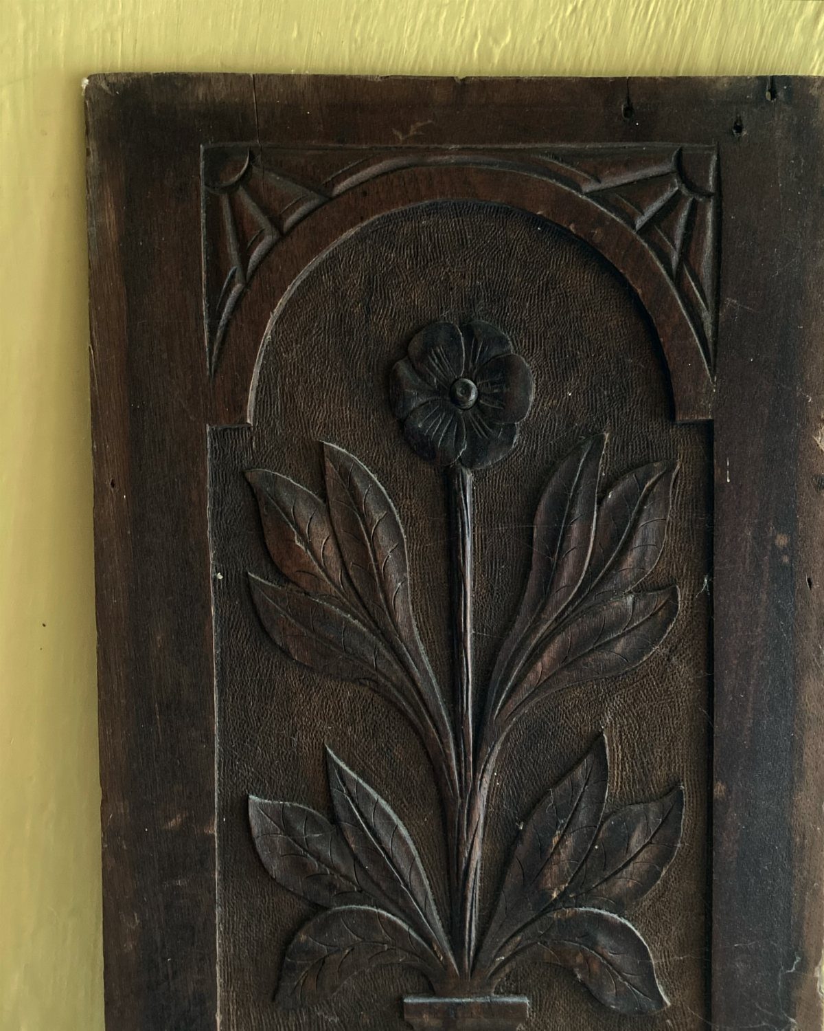 Carved wooden panel with a floral design set inside a decorative arched frame.