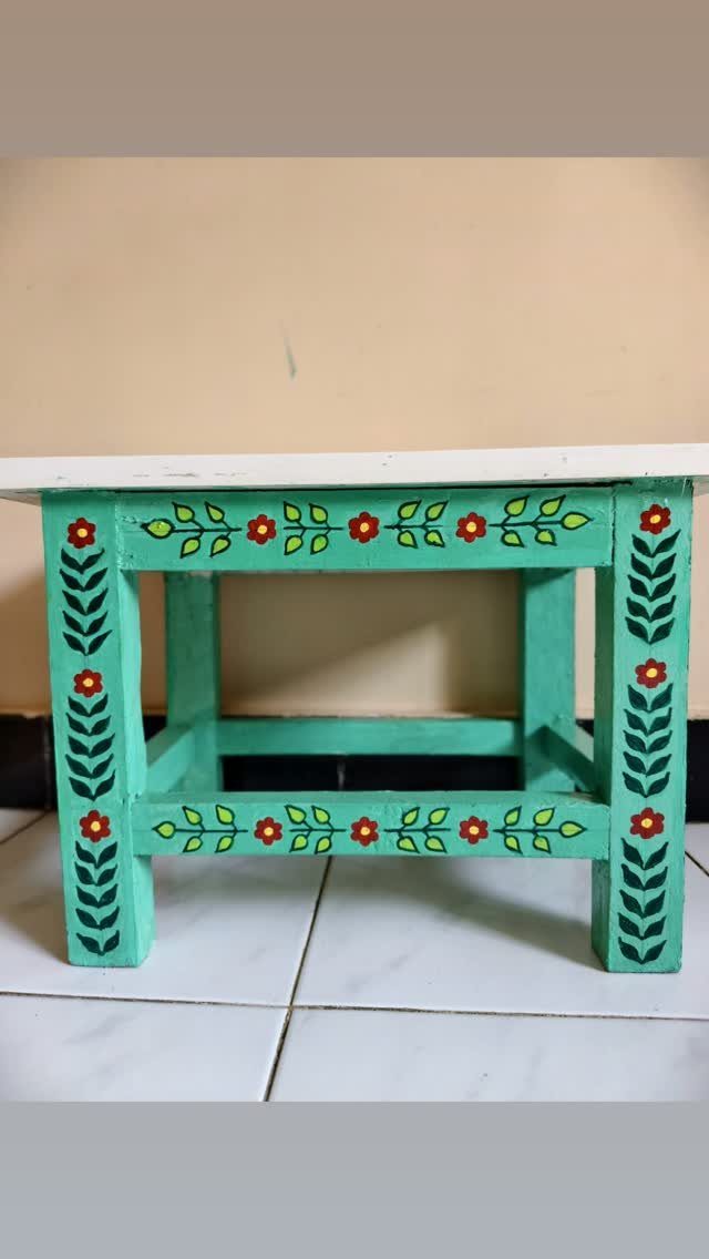 Turquoise wooden table with red and yellow painted floral designs on its legs.