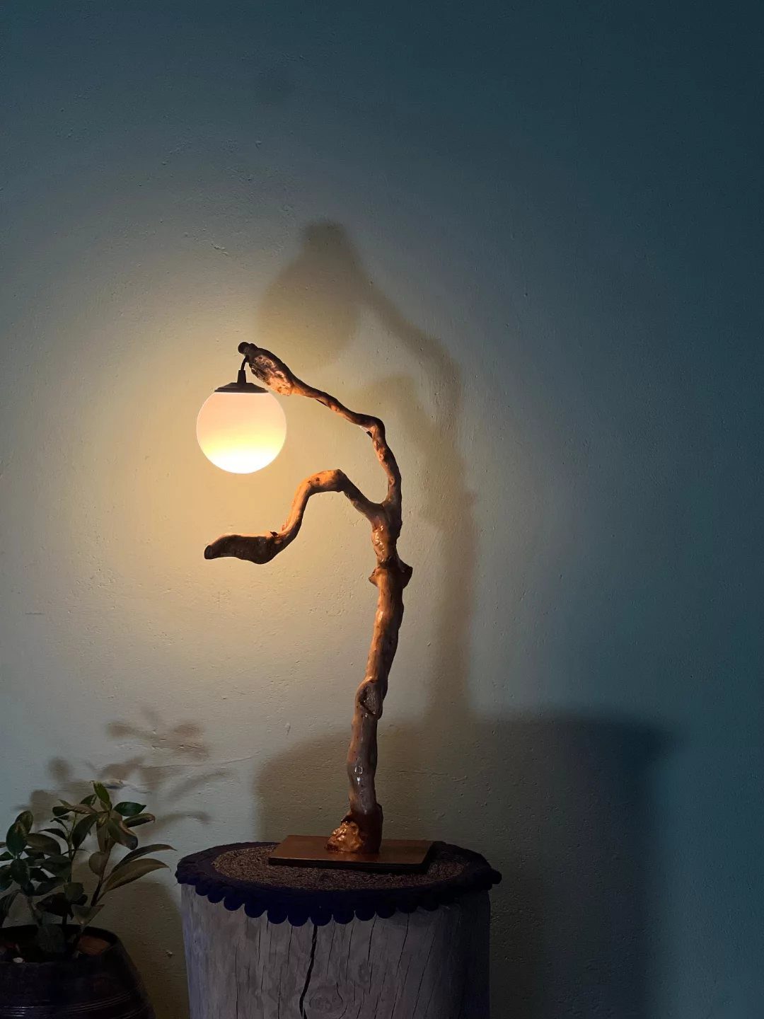 Wood Lamp Design: 14 Table, Floor and Pendant Ideas 9 Curved tree branch table lamp with a glowing white spherical bulb on a stump.