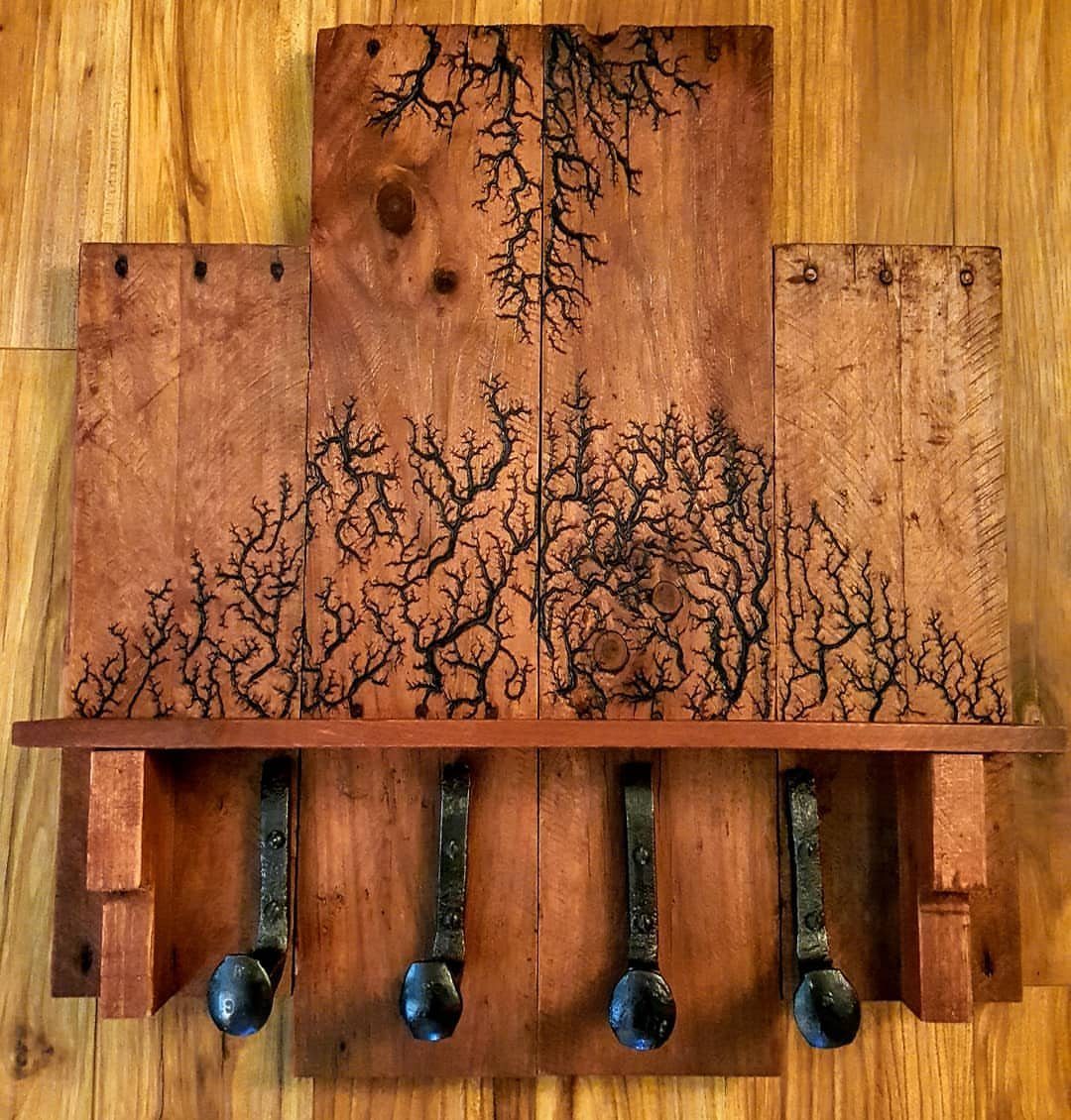 17 Wood Pallet Projects for Furniture, Decor, and Garden 6 Wooden pallet coat rack with burnt branch designs and four black metal hooks.