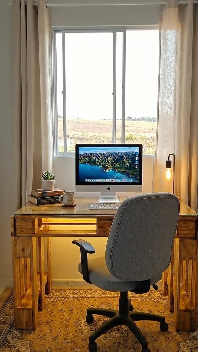 17 Wood Pallet Projects for Furniture, Decor, and Garden 10 Wooden pallet desk with a computer and grey office chair in a bright room.