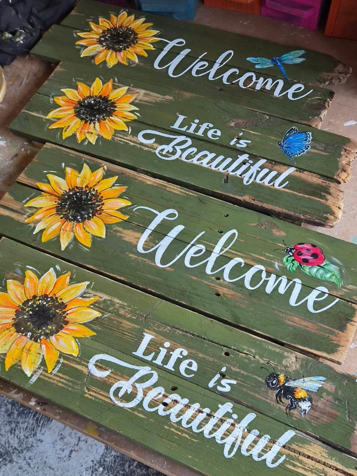 17 Wood Pallet Projects for Furniture, Decor, and Garden 15 Green pallet wood signs with painted sunflowers, insects, and cursive inspirational text.