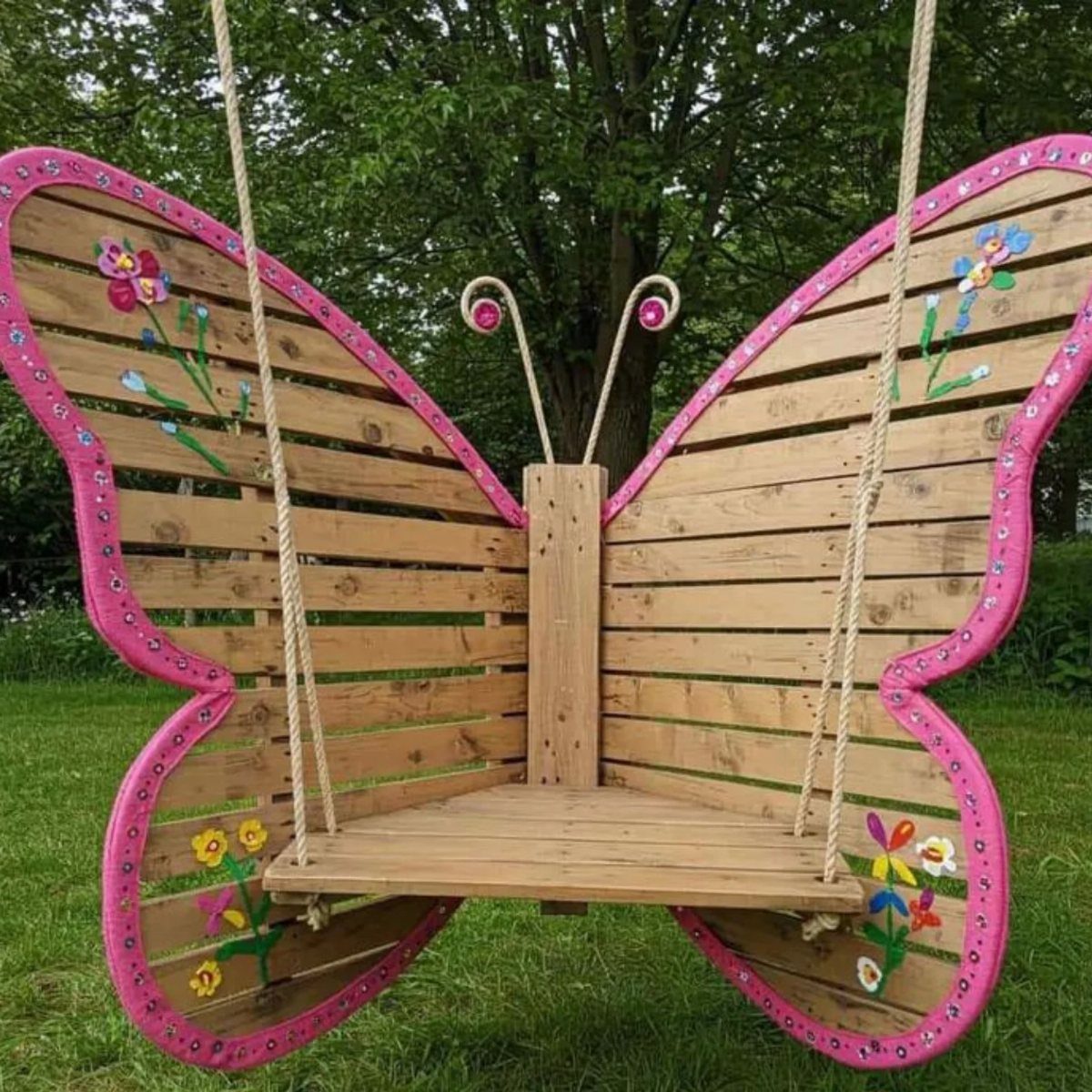 17 Wood Pallet Projects for Furniture, Decor, and Garden 2 Butterfly shaped pallet swing with pink edges and flowers in a green garden