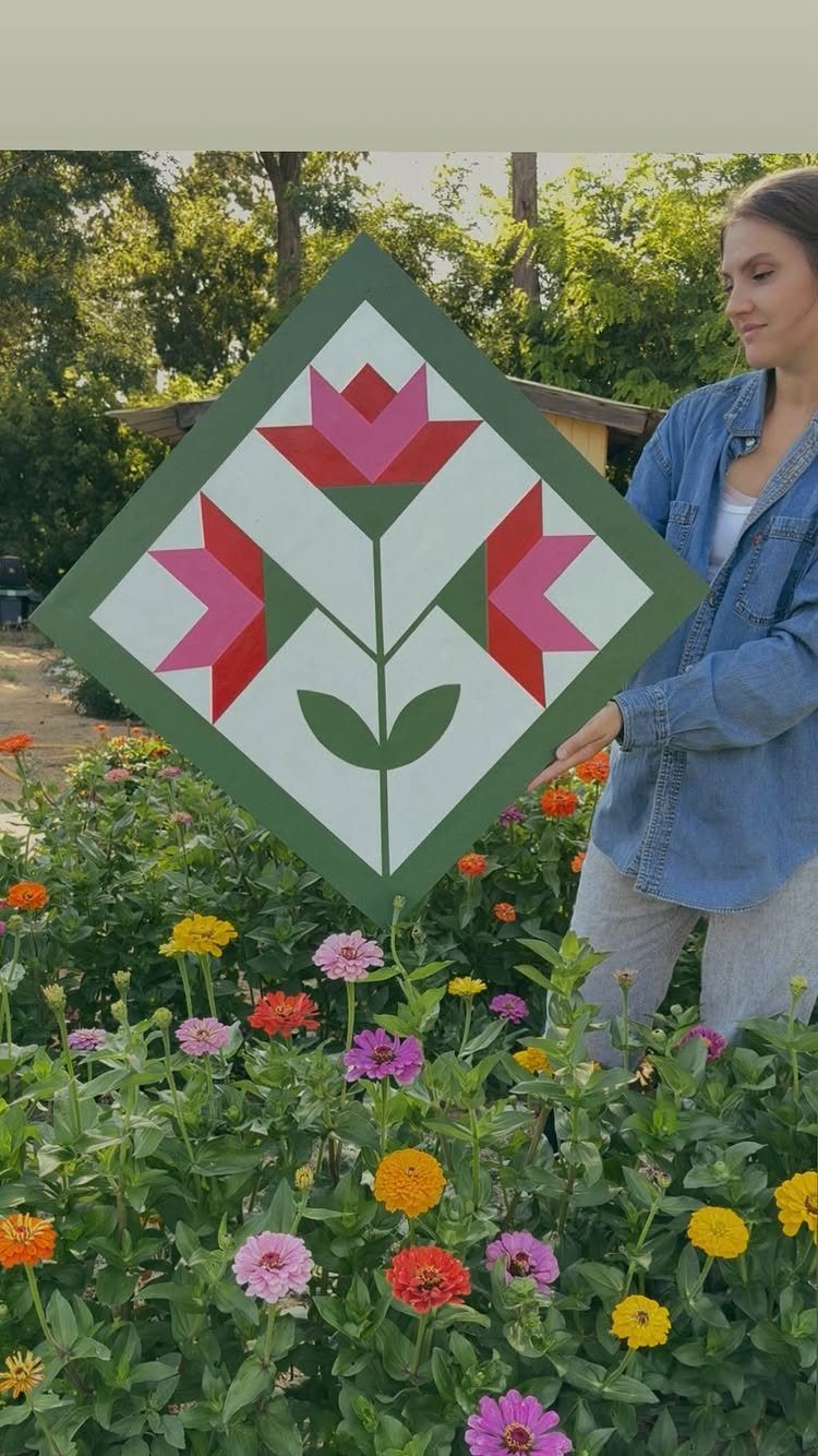 Wood Piece Art Ideas: 25 Designs for Walls and Shelves 10 Diamond-shaped wooden barn quilt art with pink flower design held in a garden.